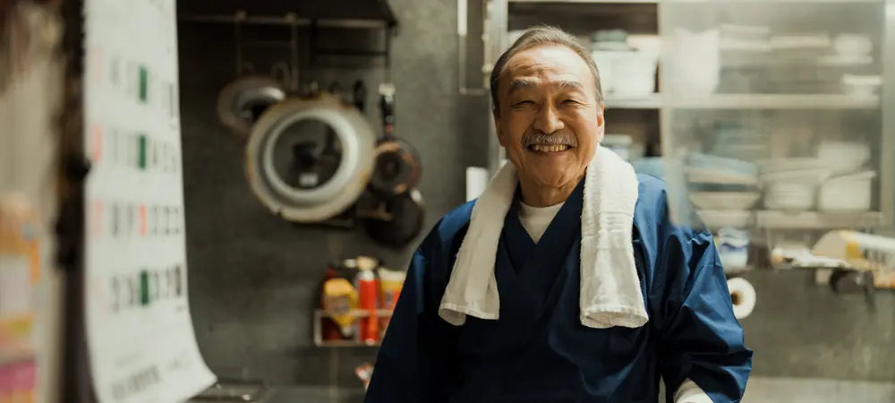 Chef japonais heureux et souriant, symbole de la transmission, du respect et de l’héritage que Damasora honore.