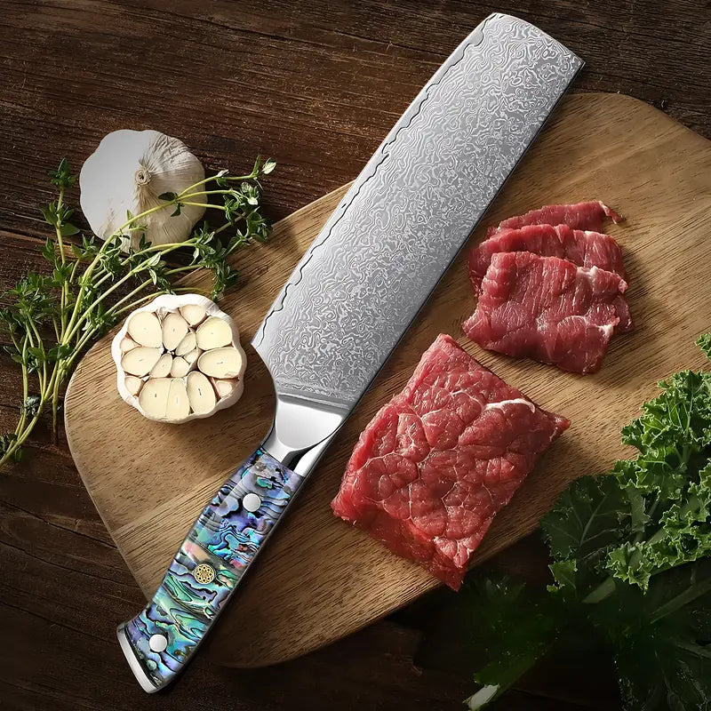 Couteau Nakiri Lame Céleste en acier damassé entouré d’ail et de viande crue sur planche ronde.