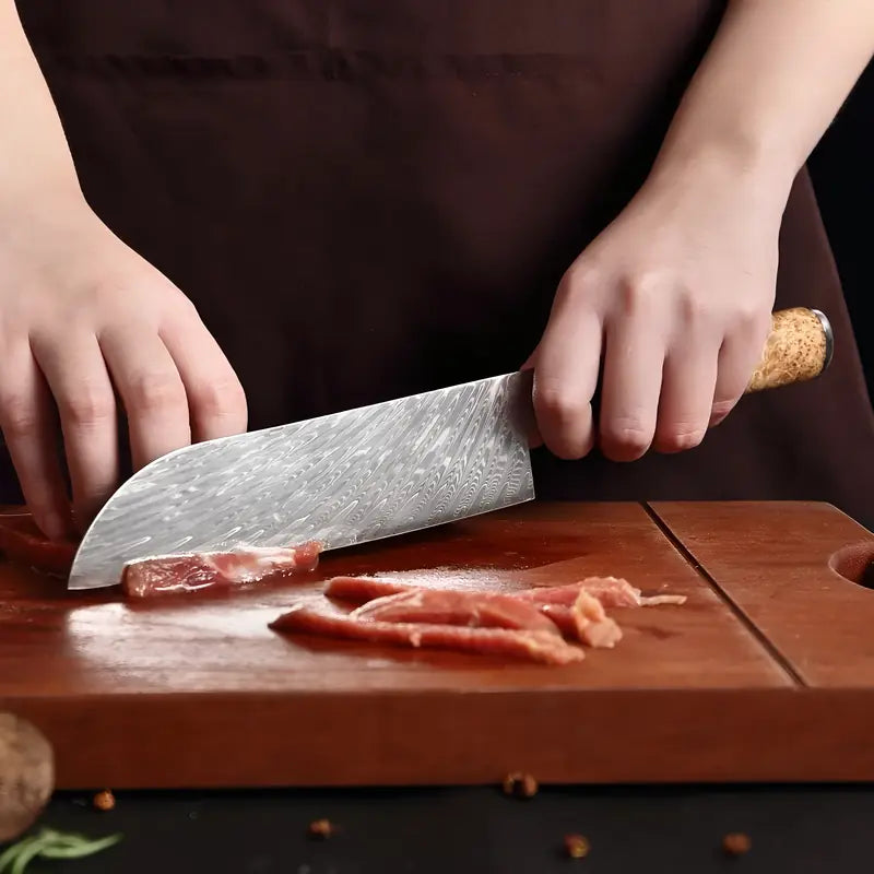 Couteau Santoku en acier damas utilisé pour trancher finement de la viande sur une planche de cuisine.
