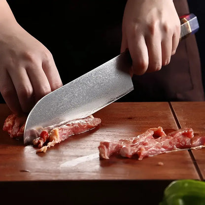 Couteau Santoku en acier damas 67 couches utilisé pour trancher de la viande sur une planche.