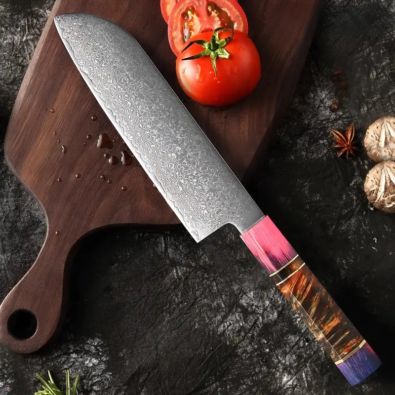 Couteau Santoku en acier damas 67 couches posé sur une planche avec des tomates et de l’ail.