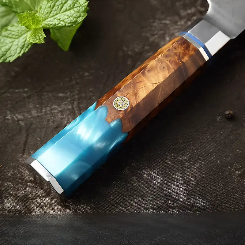Gros plan sur le manche en bois stabilisé bleu du couteau Santoku en acier damas 67 couches.