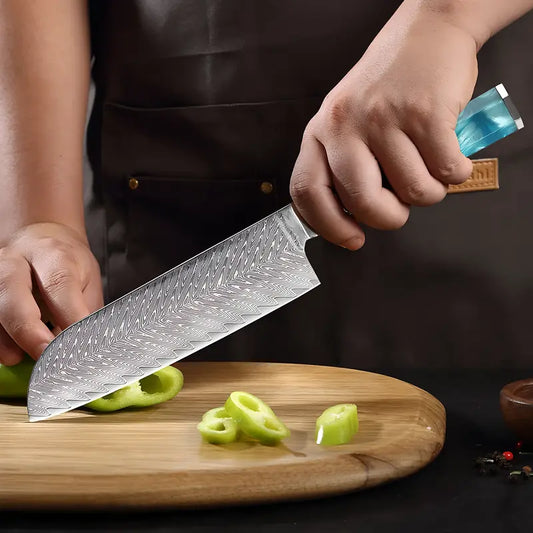 Couteau Santoku avec un manche Bleu en acier damas 67 couches utilisé pour couper un légume vert sur une planche en bois.
