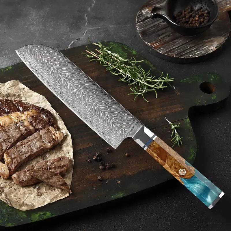 Couteau Santoku en acier damas 67 couches posé à côté d’une pièce de viande grillée et de fines herbes.