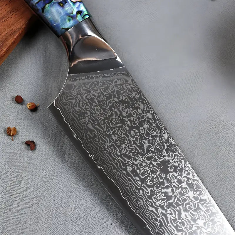 La lame damassée du couteau est photographiée sur une surface grise.