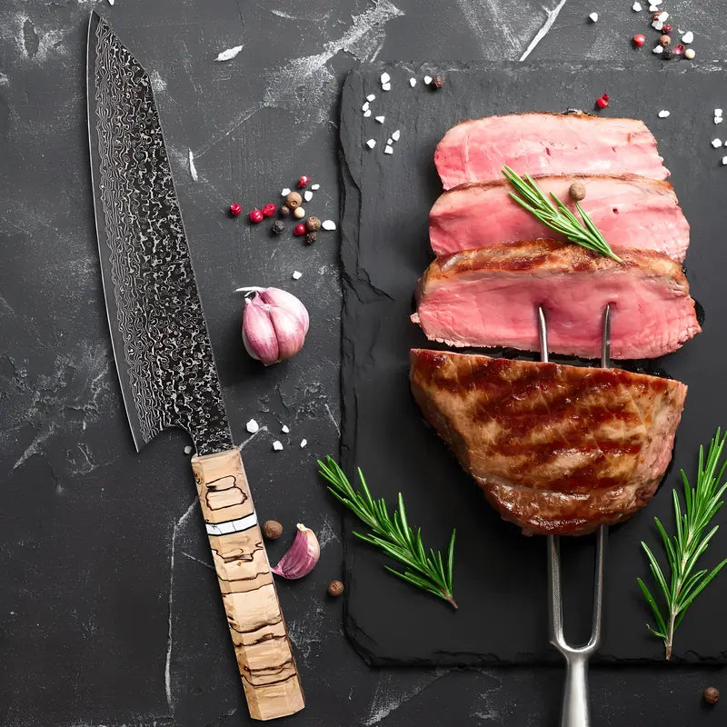 Kiritsuke Chef de l’Ombre posé à la verticale à côté d’un morceau de viande, lame damas foncée en évidence.