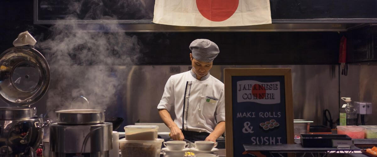 Chef japonais préparant des sushis avec un couteau traditionnel sous un drapeau du Japon